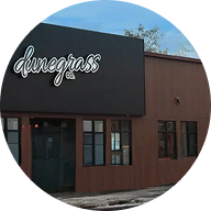 A brown building with large windows and a black sign that reads dunegrass in white script lettering above the entrance, inviting visitors to explore premium cannabis products inside.